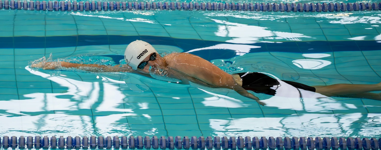 Hai Five - Schwimmschule - Ein Schwimmer mit weißer Arena-Badekappe und Schwimmbrille übt Kraulen in einer Schwimmbahn.
