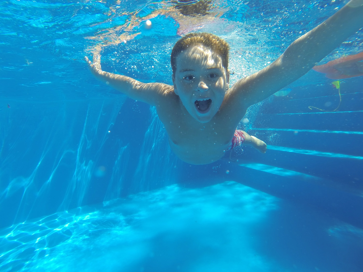 Hai Five - Schwimmschule - Ein kleiner Junge lernt schwimmen in einem hellblauen Schwimmbecken.